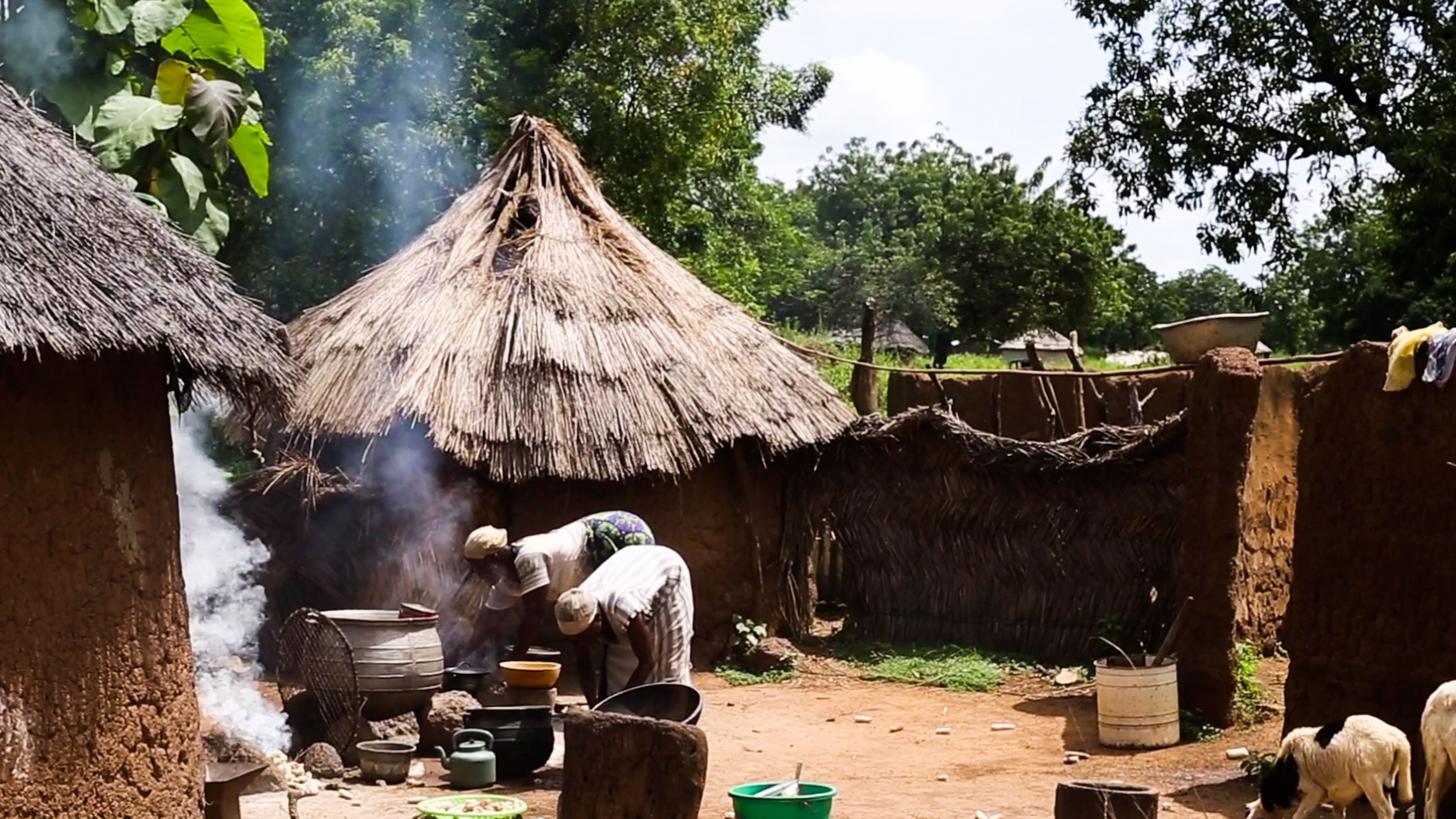 Two women cook over outdoor stoves in a Ghanaian village
