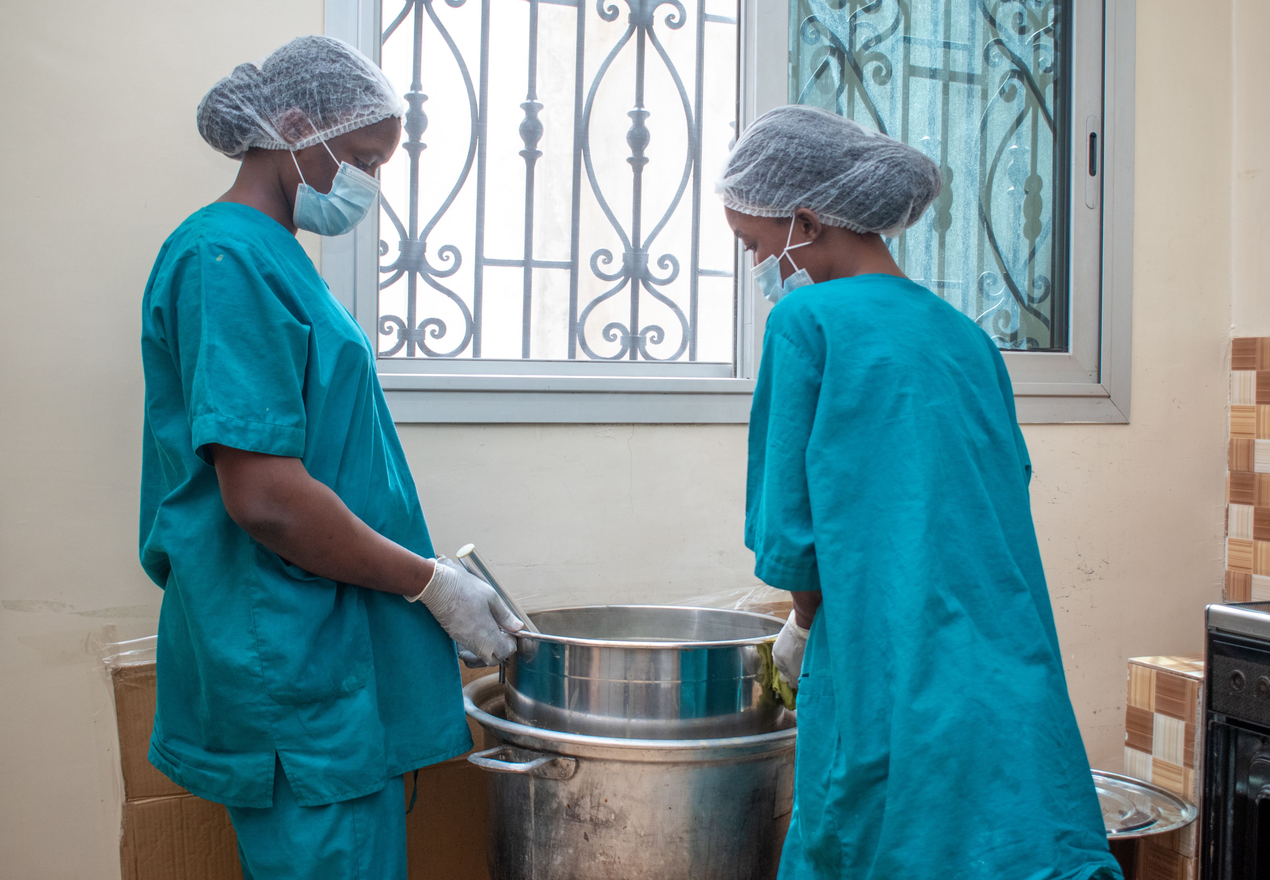 Two women stir juice in a small kitchen.